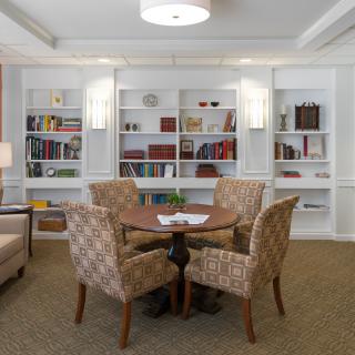 A cozy library space with bookshelves, a round table, and four patterned chairs.