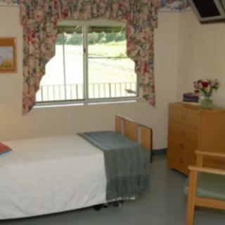 A simple hospital room with a single bed, window, and basic furnishings.