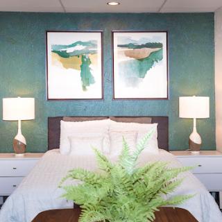 A serene and stylish bedroom featuring a calming teal wall, contemporary artwork, and inviting furnishings.