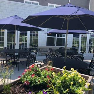 Sunny outdoor patio area with tables, chairs, and flower garden.