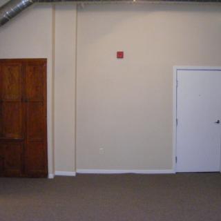 An empty room with two doors, one wooden and one white, on a carpeted floor.
