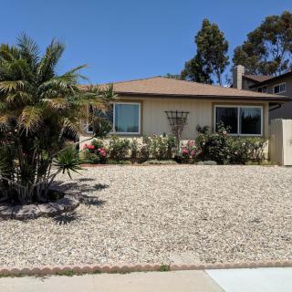 A single-story house with a gravel yard and palm trees, set under a clear blue sky.