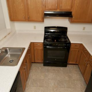 A compact kitchen with wooden cabinets, a black stove, and a stainless steel sink.