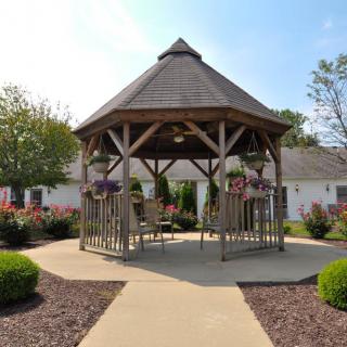 A wooden gazebo surrounded by a landscaped garden with flowers and well-kept pathways.