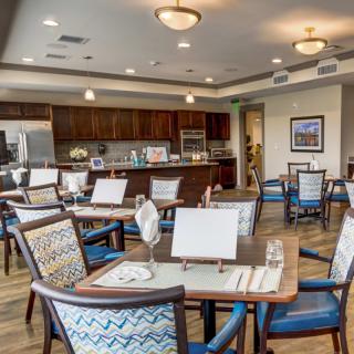 A modern dining area with neatly arranged tables and chairs, featuring a kitchen in the background.