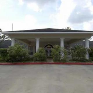 A building with a covered entrance supported by columns and surrounded by greenery.