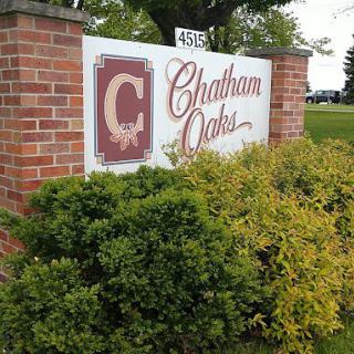 A sign for Chatham Oaks mounted on a brick wall, surrounded by shrubs.