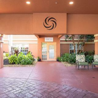 The image shows an entrance area with outdoor seating, featuring plants and distinctive architectural design.