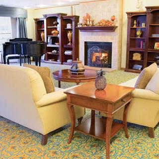 A cozy living room featuring comfortable seating, a fireplace, bookshelves, and a grand piano.