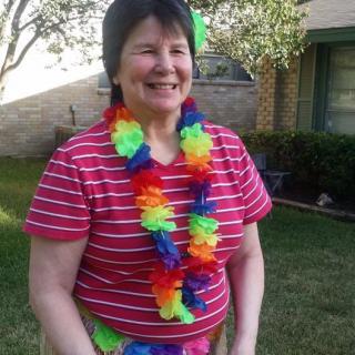 A woman smiling outdoors, wearing a striped shirt and a colorful lei.