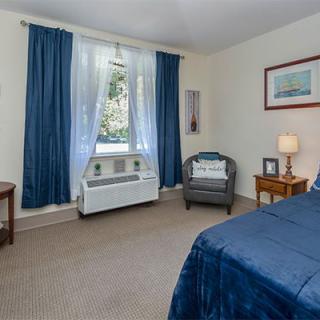 A cozy bedroom featuring blue curtains, an armchair, and a neatly made bed.