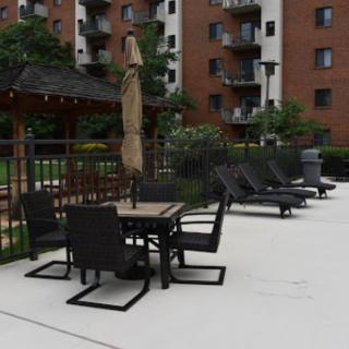 A patio area with chairs, tables, and an umbrella in front of an apartment building.