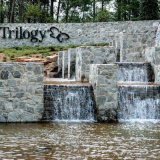 Stone wall with water cascading down multiple levels, featuring a sign that reads 'Trilogy'.