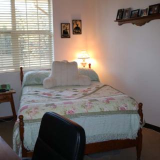 A cozy bedroom with a single bed, decorated with floral bedding and illuminated by a bedside lamp.