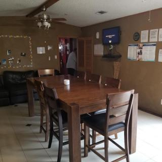 A cozy dining room with a large wooden table and chairs, featuring brown walls and a mounted television.