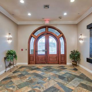 A well-lit interior entrance with an arched wooden door and tile flooring, accented by plants and wall sconces.