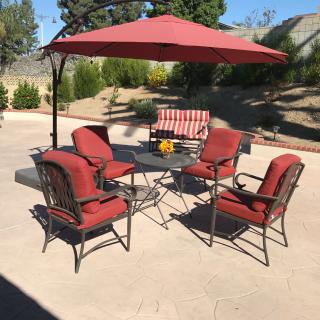 A patio setup with red cushioned chairs, a table, and a large umbrella on a sunny day.