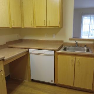 A compact kitchen featuring yellow cabinets, a countertop, sink, and a dishwasher.