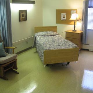 A simple and functional hospital room featuring a single bed, a chair, and a lamp.