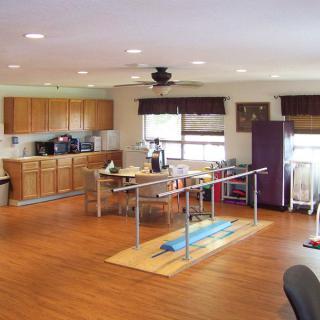 A spacious rehabilitation room equipped with parallel bars and a kitchenette for physical therapy sessions.