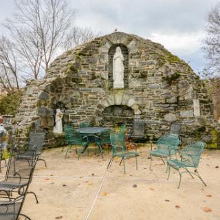 A serene view of a stone ruin featuring a statue, surrounded by outdoor seating.