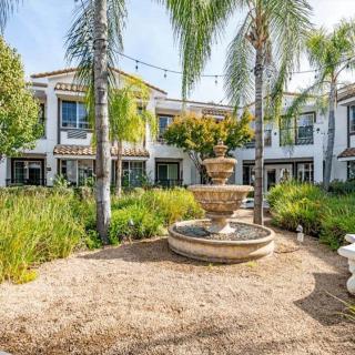 A beautiful house with a central courtyard featuring a multi-tiered fountain surrounded by palm trees and lush garden landscaping.