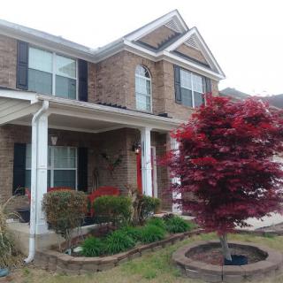 A brick house with a covered porch and landscaped front yard featuring a red tree.