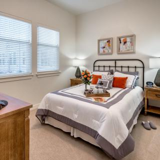 A cozy bedroom with a neatly made bed, adorned with pillows and surrounded by wooden furniture and decorative artwork.