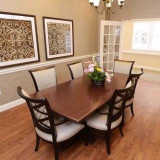 A well-decorated dining room featuring a wooden table with six chairs, framed artwork on the walls, and a hardwood floor.