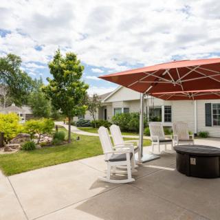A cozy patio setup with chairs and an umbrella, surrounded by a well-maintained garden on a sunny day.