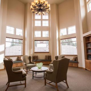 A cozy library seating area with comfortable chairs, large windows, and a chandelier.