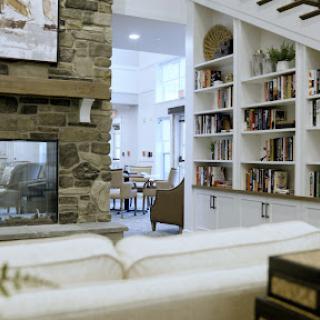 A cozy living room featuring a stone fireplace and built-in bookshelves, illuminated by natural light.