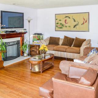 A cozy living room with a sofa, armchair, and fireplace, featuring elegant plants and artwork.