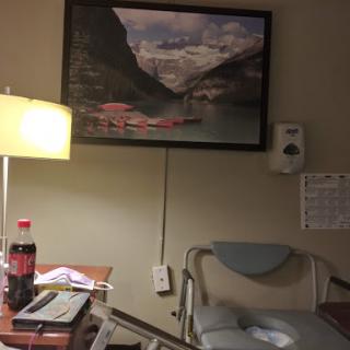 A hospital room featuring a lamp, a small table with personal items, and a landscape painting on the wall.