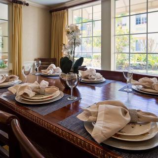 An elegantly set dining table in a sunlit room, adorned with flowers and neatly arranged napkins.