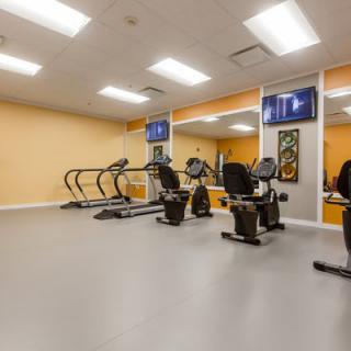 A well-lit gym with various fitness equipment including treadmills and stationary bikes.