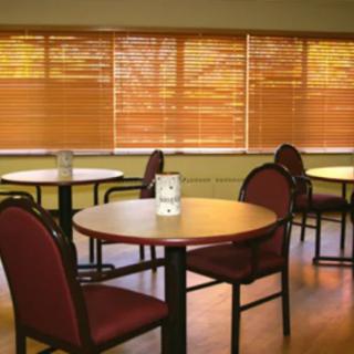An empty cafe with round tables and chairs near window blinds.
