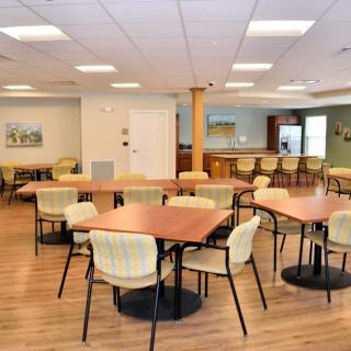 A spacious dining area with neatly arranged tables and chairs, featuring a wooden floor and bright lighting.