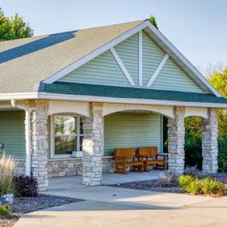 A quaint house with a green facade and stone pillars surrounding the porch.