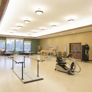 A spacious rehabilitation room equipped with parallel bars and exercise equipment for physical therapy.