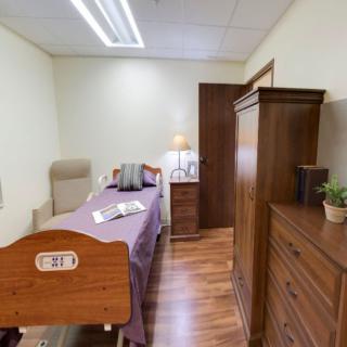 A cozy bedroom with a hospital bed, armchair, and wooden furniture.