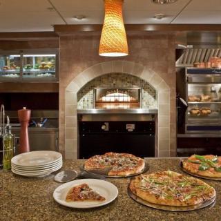 A restaurant kitchen with pizzas displayed on the counter and a wood-fired oven in the background.