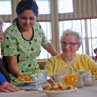 A caregiver assists elderly residents during a meal at a nursing home.
