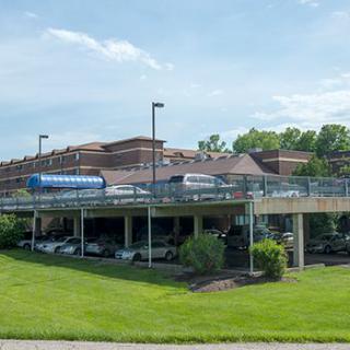 A hospital building with a parking area beneath and surrounding greenery.