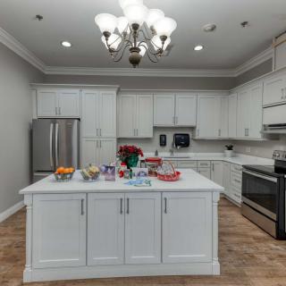 A modern kitchen with white cabinets and a central island, featuring stainless steel appliances and a decorative chandelier.