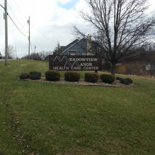 A welcoming sign located on a grassy hill, surrounded by landscaping and under a cloudy sky.