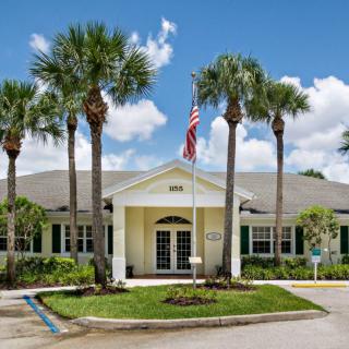 A well-maintained building with palm trees and an American flag on a sunny day.