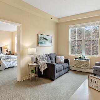 A cozy and bright apartment interior featuring a living room with a sofa and a view into the bedroom.