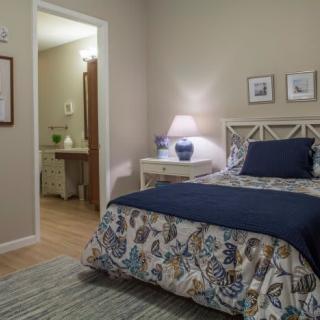 A cozy bedroom with a single bed, decorative comforter, and a lamp on the nightstand.