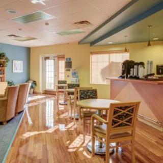 A cozy lobby interior with wooden flooring, featuring a seating area, reception desk, and coffee station.
